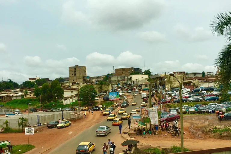 small town road with lots of cars and some parked on the right side and buildings in the background